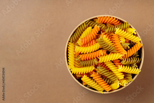 Tricolor fusilli pasta in a cardboard box. Raw fusilli pasta on a beige background. Copy space