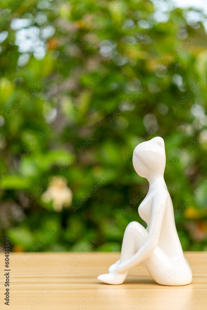 Ceramic Yoga Figurine of Woman doing yoga pose on wooden floor and green leaf background Ceramic Yoga Figurine of Woman doing yoga pose on wooden floor and green leaf background
