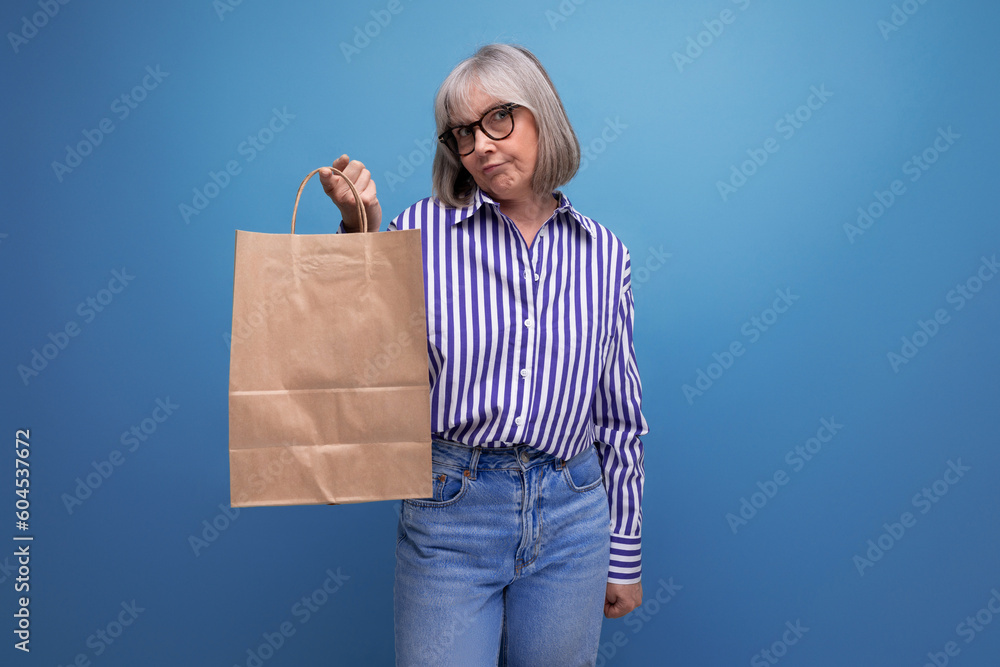 fashionable middle aged woman with gray hair holding social help package on bright studio background with copy space fashionable middle aged woman with gray hair holding social help package on bright studio background with copy space