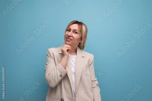 pensive blond millennial woman in stylish jacket thinks about business on studio background with copy space
