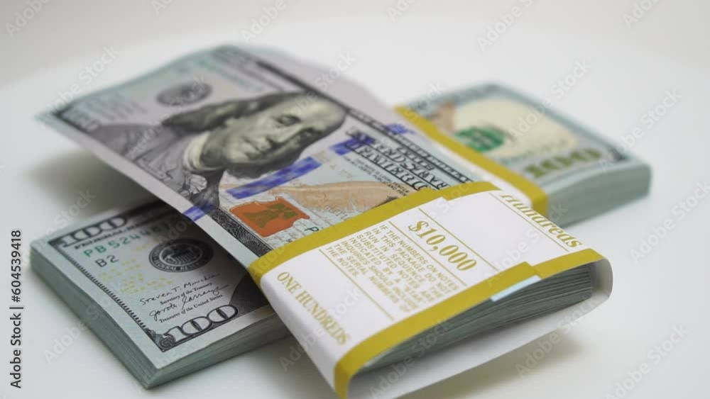 stack of bank bundles with US dollars on a white background. Close-up shot of new, freshly printed hundred-dollar bills rotating on a table. cash flow, business investment, or big money concepts. stack of bank bundles with US dollars on a white background. Close-up shot of new, freshly printed hundred-dollar bills rotating on a table. cash flow, business investment, or big money concepts.