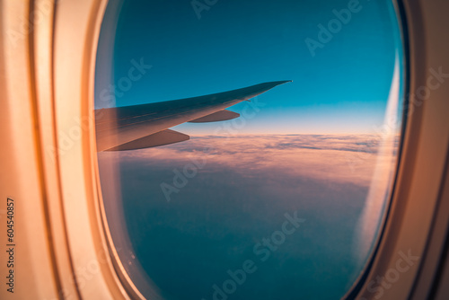Beautiful aerial view from aircraft passenger cabin on red orange sunrise cloudscape and blue sky. Plane wing from airplane window seat in flight nature landscape against scenic sunset sky background