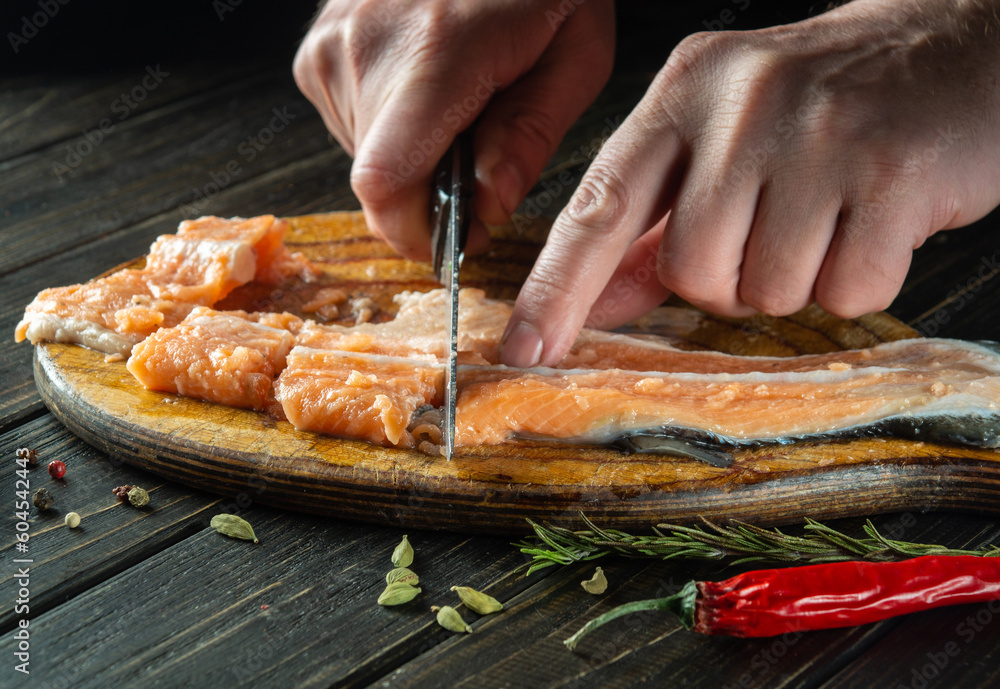 The cook cuts fresh red trout fish with a knife on a kitchen cutting board. Cooking a delicious fish dish according to an old recipe with spices