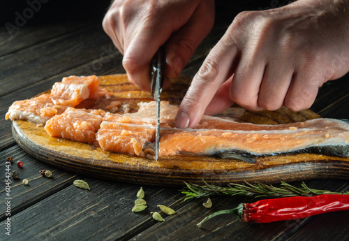 The cook cuts fresh red trout fish with a knife on a kitchen cutting board. Cooking a delicious fish dish according to an old recipe with spices