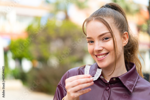 Young pretty girl at outdoors holding invisible braces with happy expression