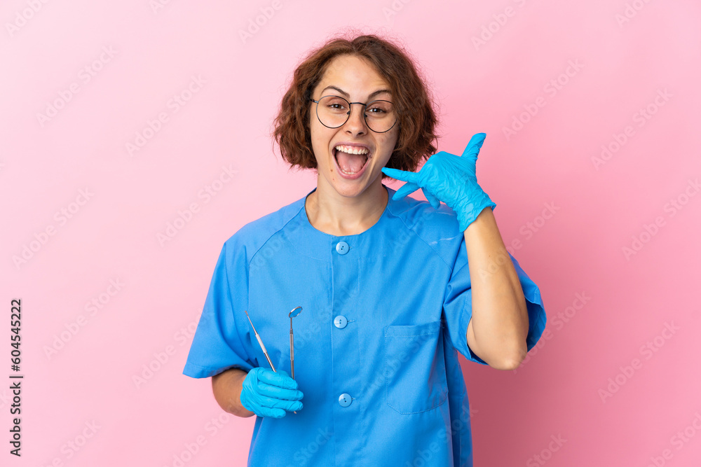Woman English dentist holding tools over isolated on pink background making phone gesture. Call me back sign Woman English dentist holding tools over isolated on pink background making phone gesture. Call me back sign