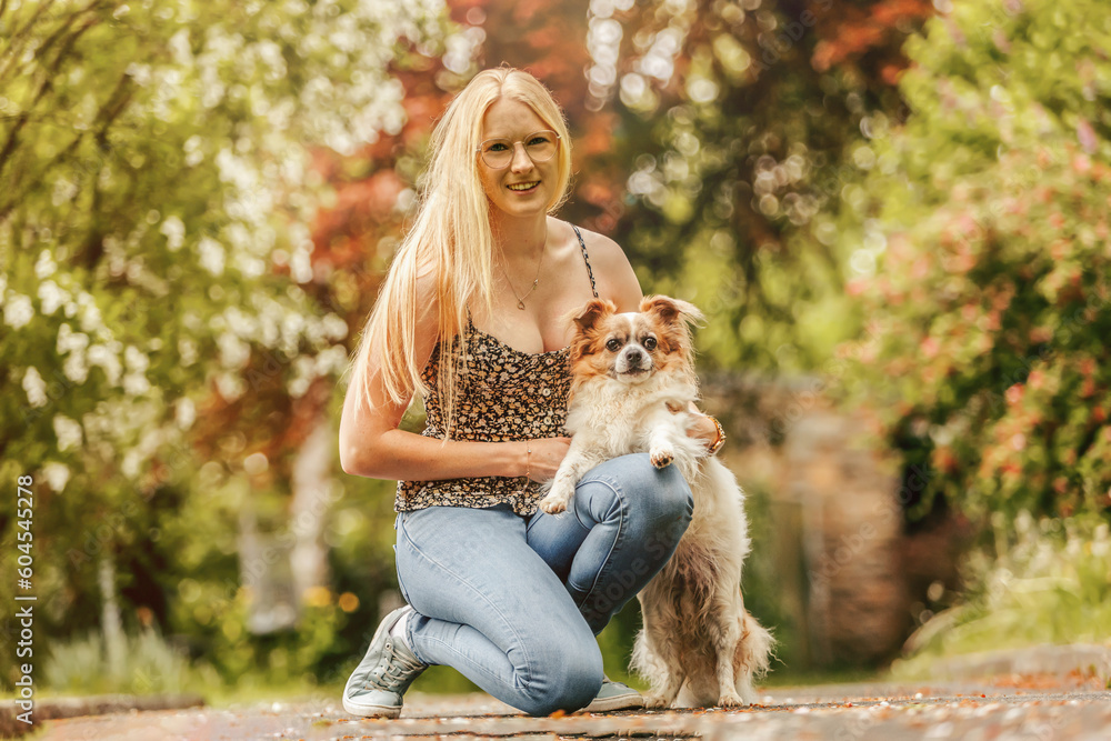 Portrait of a blonde young woman having fun with her longhaired Chihuahua dog in a park in spring outdoors Portrait of a blonde young woman having fun with her longhaired Chihuahua dog in a park in spring outdoors