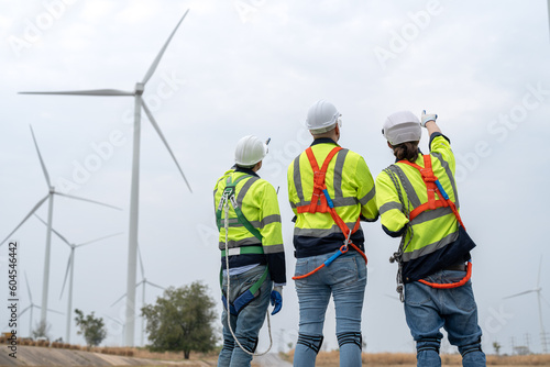 Engineers windmill team wearing uniform and helmet discussing inspection and maintenance of wind turbine in wind farms to generate electrical energy, Renewable energy.