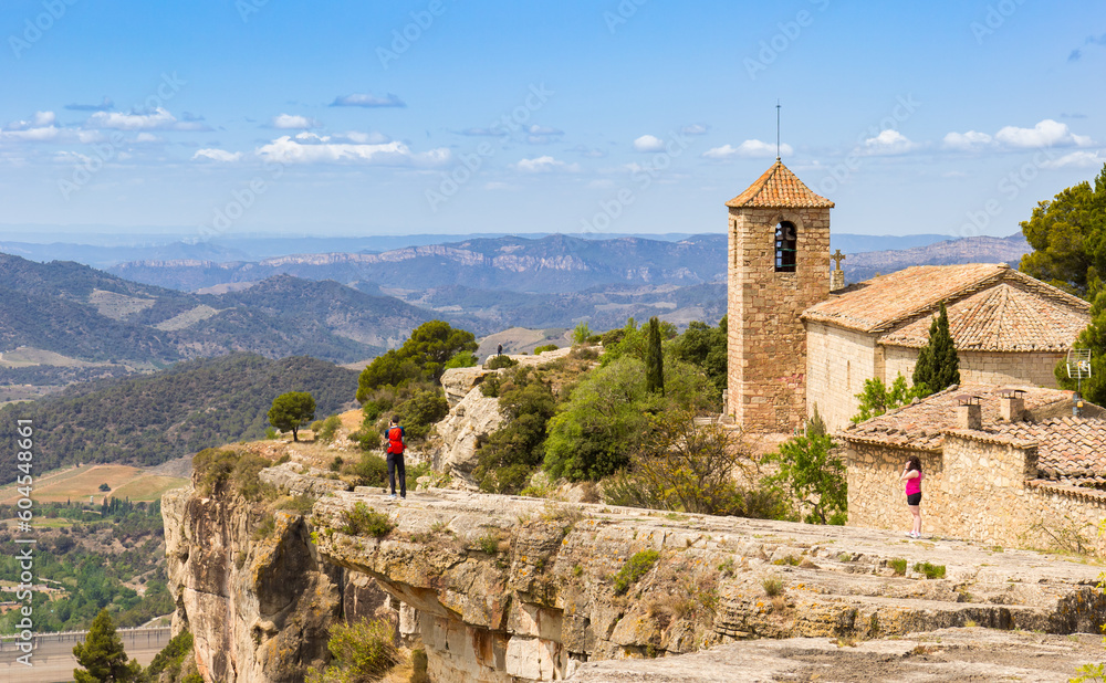 People on the cliff enjoying the view over the mountains and the church in Siurana, Spain People on the cliff enjoying the view over the mountains and the church in Siurana, Spain