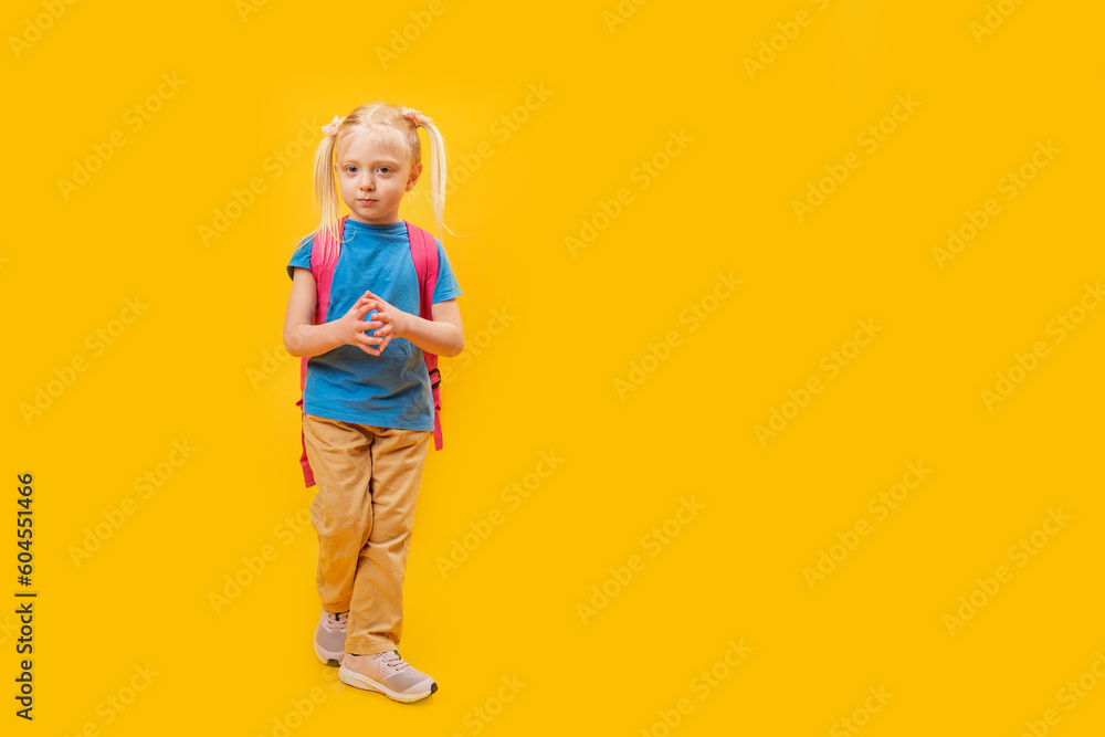 Full-length portrait of little girl with backpack on bright yellow background. Primary school student. Copy space, mock up