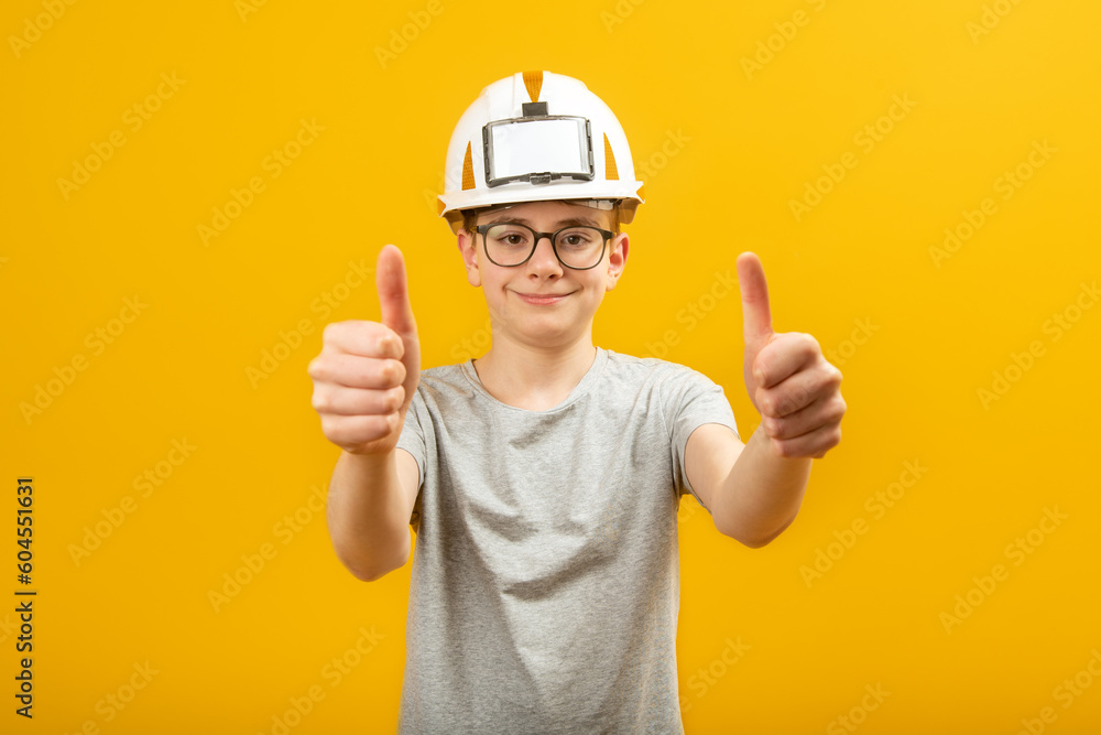 Guy with glasses wears protective helmet and shows thumbs up with two hands. Teenager shows gesture like isolated on yellow background. Guy with glasses wears protective helmet and shows thumbs up with two hands. Teenager shows gesture like isolated on yellow background.