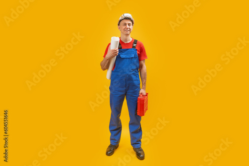 Young man engineer worker or architect with helmet holds documents blueprints and tool box. Isolated on yellow background. Copy space.