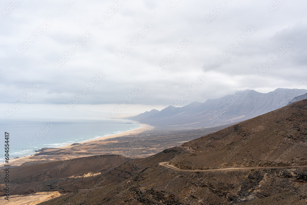 montaña rocosa con camino de tierra e inmensa playa de arena amarilla