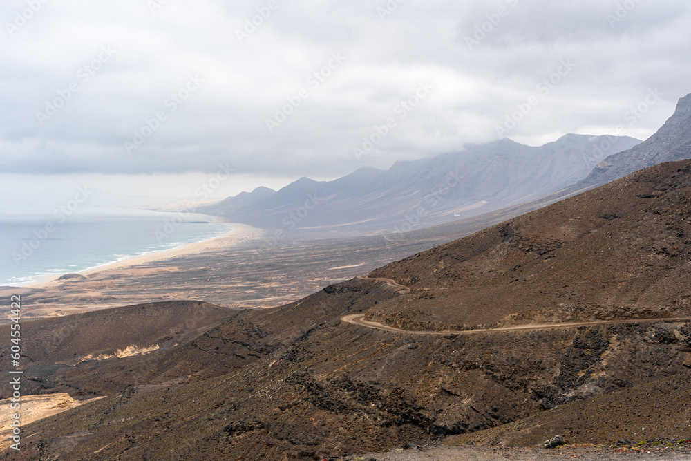 montaña rocosa con camino de tierra e inmensa playa de arena amarilla