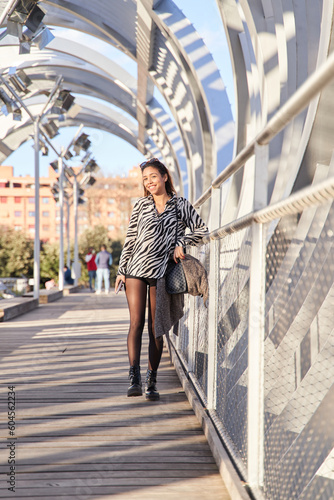 full length portrait of a latina woman on a sunny day in the city, looking at the camera with her mobile phone in her hand.