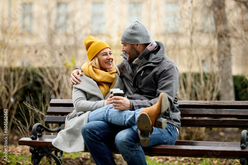 Couple drinking hot beverage sitting on park bench in the winter outdoors