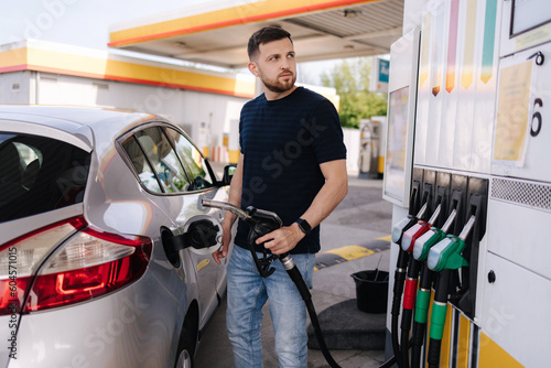 Handsome bearded man refueling car and looking on the scoreboard while standing on self service gas station
