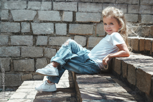 Tableau sur toile A little toddler girl sitting on the stairs and posing in jeans and white shirt