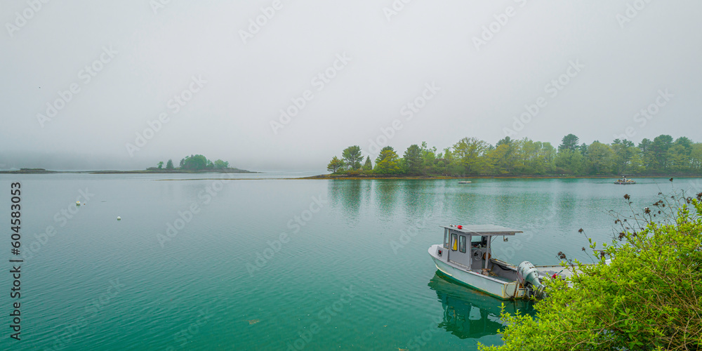 The moored trawler, trees on islands, and water reflections on the calm seawater. Tranquil Maine coastal road seascape over Casco Bay on Bailey Island on a foggy morning. The moored trawler, trees on islands, and water reflections on the calm seawater. Tranquil Maine coastal road seascape over Casco Bay on Bailey Island on a foggy morning.