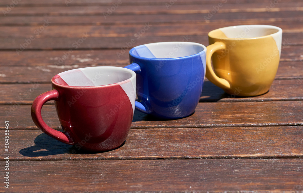 Tea time. Family time. Three multi colored cups on a wooden brown table Tea time. Family time. Three multi colored cups on a wooden brown table