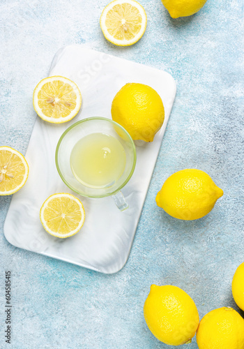 A cup of squeezed lemon juice and lemons, slices of lemons around. Bright background. Summer concept