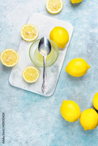 A cup of squeezed lemon juice and lemons, slices of lemons around. Bright background. Summer concept