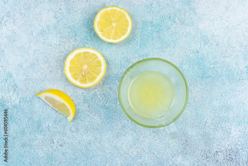 A cup of squeezed lemon juice and lemons, slices of lemons around. Bright background. Summer concept
