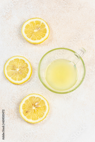 A cup of squeezed lemon juice and lemons, slices of lemons around. Bright background. Summer concept