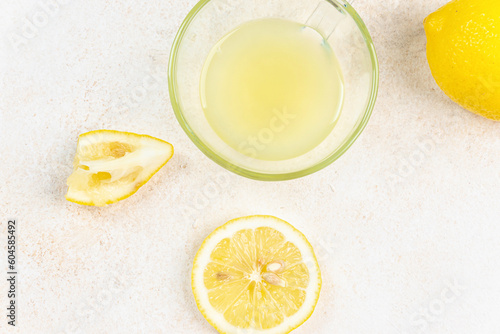 A cup of squeezed lemon juice and lemons, slices of lemons around. Bright background. Summer concept