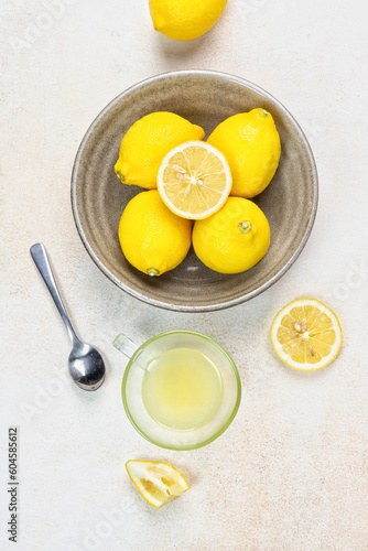A cup of squeezed lemon juice and lemons, slices of lemons around. Bright background. Summer concept