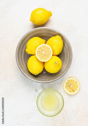 A cup of squeezed lemon juice and lemons, slices of lemons around. Bright background. Summer concept