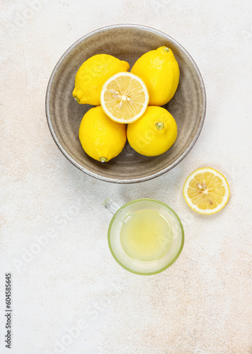 A cup of squeezed lemon juice and lemons, slices of lemons around. Bright background. Summer concept