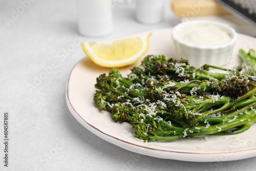 Tasty cooked broccolini with cheese, lemon and sauce on light table, closeup. Space for text photo