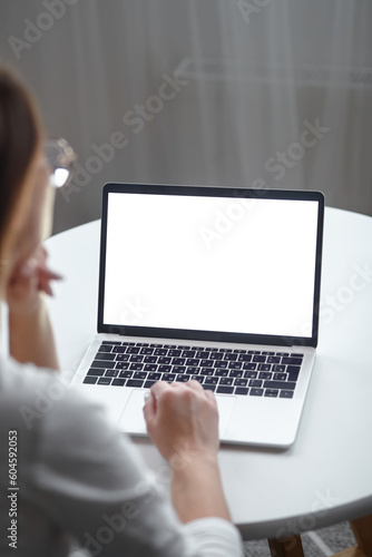 Mockup white screen laptop woman using computer while sitting at table at home, back view