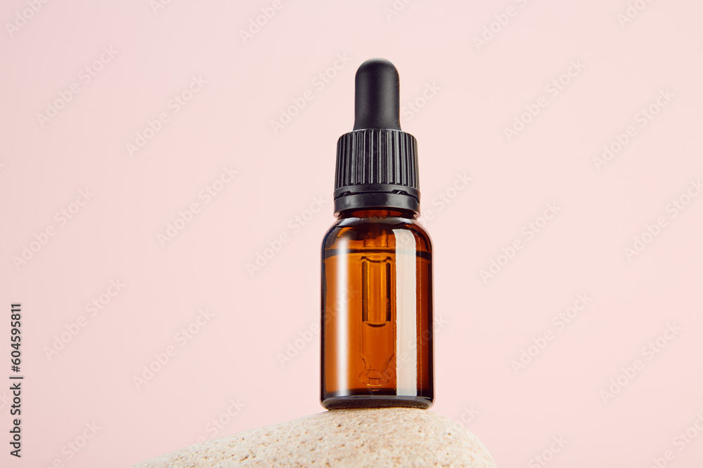 Glass amber vial on spa stone on pink background. Glass amber vial on spa stone on pink background.