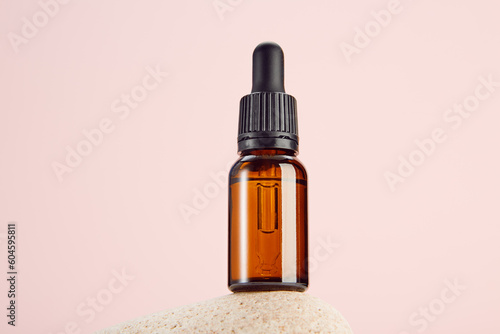 Glass amber vial on spa stone on pink background.
