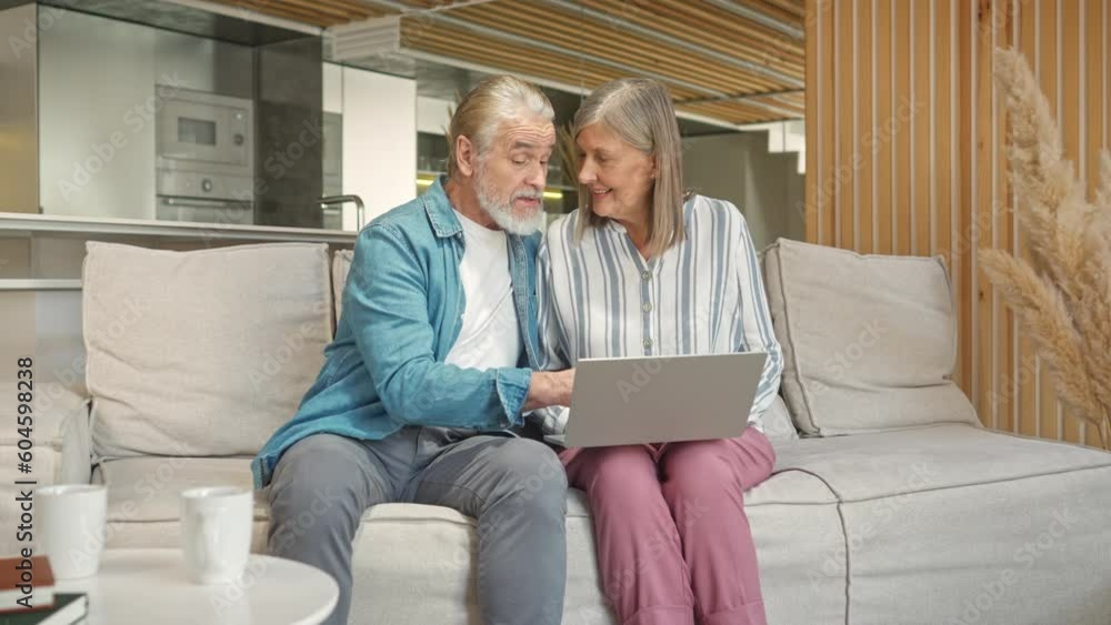 Adult Caucasian parents relaxing while sitting on soft couch in living room. Pretty woman using laptop and searching on websites some information while her husband helping her and telling what to do. Adult Caucasian parents relaxing while sitting on soft couch in living room. Pretty woman using laptop and searching on websites some information while her husband helping her and telling what to do.