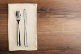 Shiny fork, knife and napkin on wooden table, top view. Space for text