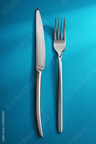 Shiny fork and knife on light blue background, flat lay