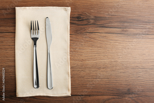Shiny fork, knife and napkin on wooden table, top view. Space for text