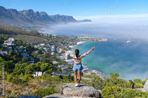 women with hands up at The Rock viewpoint in Cape Town over Campsbay, view over Camps Bay with fog over the ocean. fog coming in from the ocean at Camps Bay Cape Town South Africa