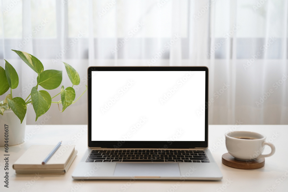 Laptop and notebooks and coffee cup and plant on wooden table in front of window