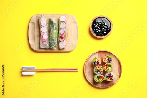 Different delicious spring rolls, chopsticks and soy sauce on yellow background, flat lay