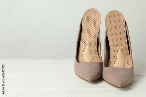 Orthopedic insoles in high heel shoes on white wooden floor, closeup. Space for text