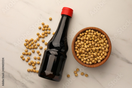 Bottle of soy sauce and soybeans on white marble table, flat lay