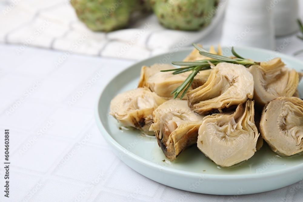 Plate with pickled artichokes and rosemary on white tiled table, closeup