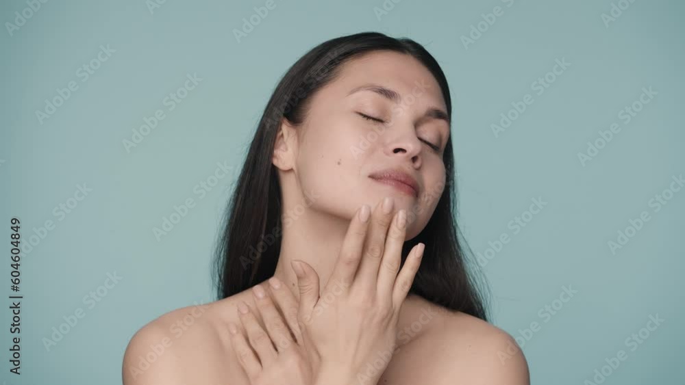 An attractive young woman runs her fingers across her face, gently touching smooth, healthy skin. Close up portrait of a woman on a blue background. Natural beauty, cosmetology, skin care. Slow motion An attractive young woman runs her fingers across her face, gently touching smooth, healthy skin. Close up portrait of a woman on a blue background. Natural beauty, cosmetology, skin care. Slow motion