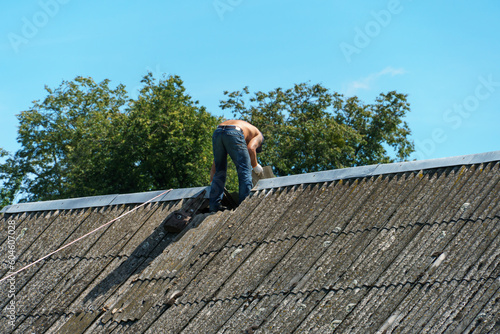 Repair of an old tiled roof. The owner of the house is trying to fix the roof on his own. A builder works on the roof of an old wooden house. © Pokoman