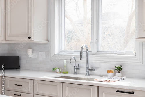 A kitchen sink detail with tan cabinets  white marble countertop  subway tile backsplash  and chrome faucet.