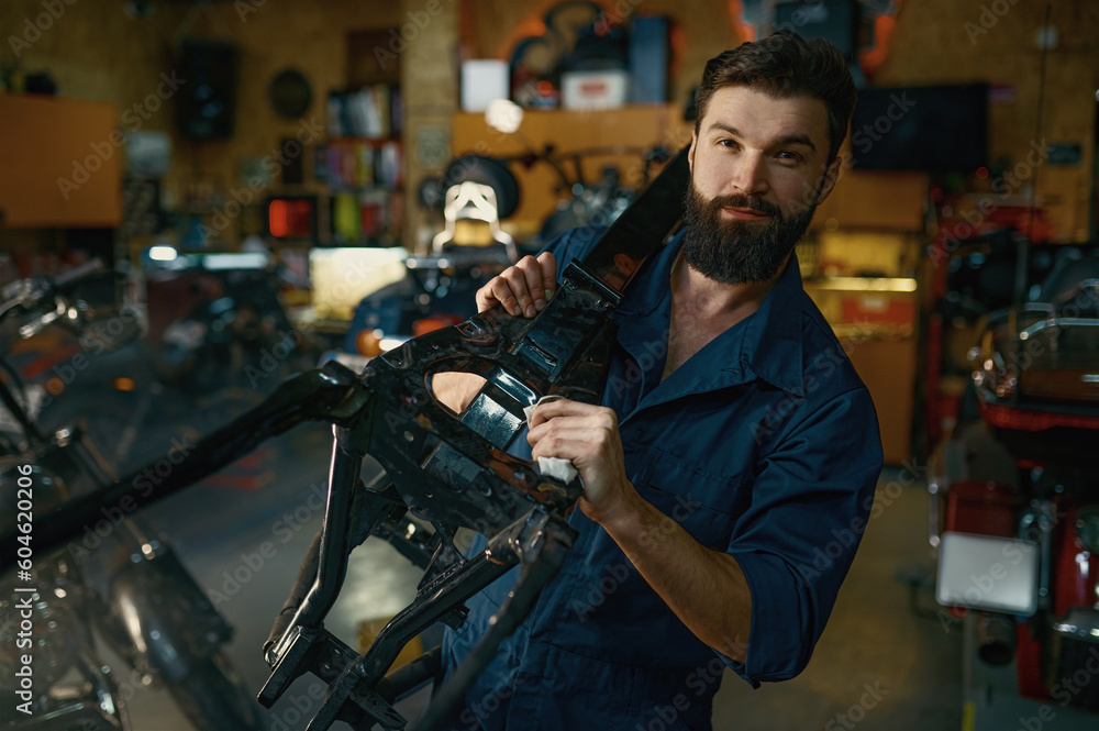 Fototapeta premium Portrait of young repairman in coveralls carrying spare part of motorcycle